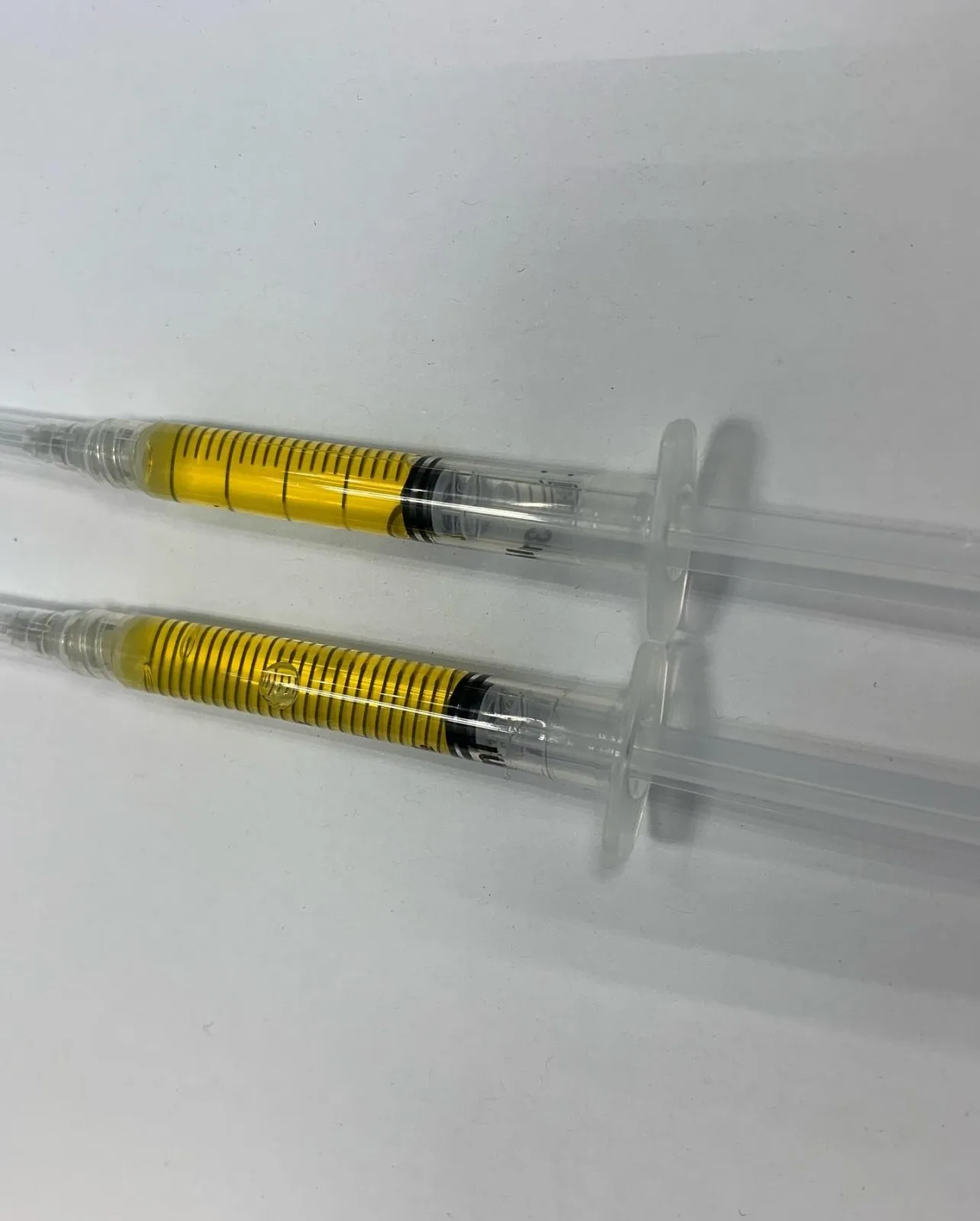 Two PRP injection syringes with yellow measurement markings on white surface
